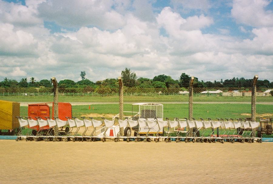 Luggage trolleys lined up against an airfield fence, Kenya. Film photograph by Nicolò Pudel