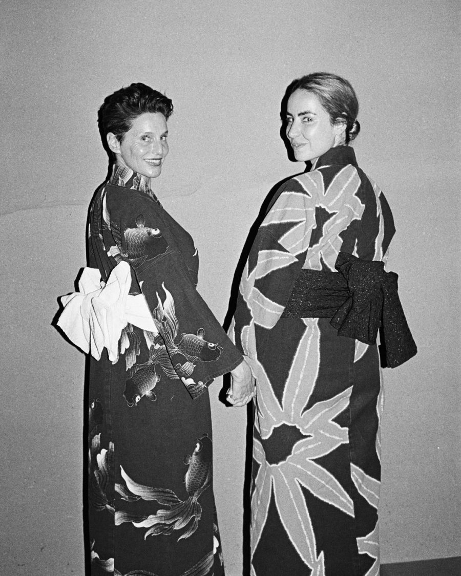 Two women wearing patterned kimonos stand back-to-back against a plain background, film photograph by Nicolò Pudel.