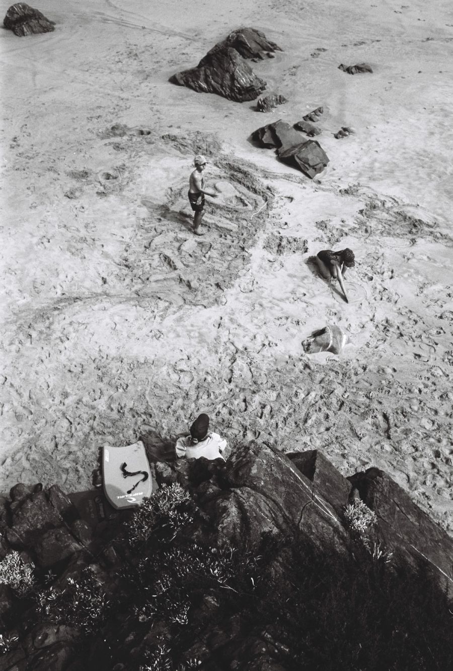 Bathers and rocks on a pale beach seen from above, black and white, Cape Town. Film photograph by Nicolò Pudel