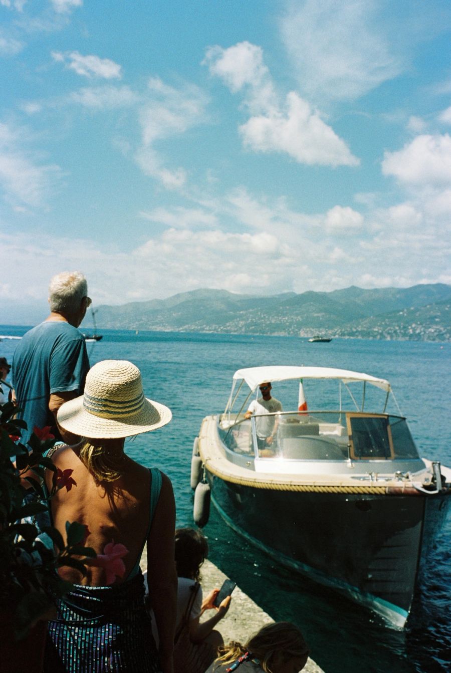 Onlookers watching a motorboat moor at the water's edge, Ligurian coast, Italy. Film photograph by Nicolò Pudel