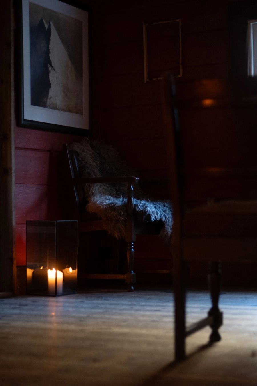 Sheepskin-draped chair and lit candles in a dim red-walled timber room, Norway. Film photograph by Nicolò Pudel