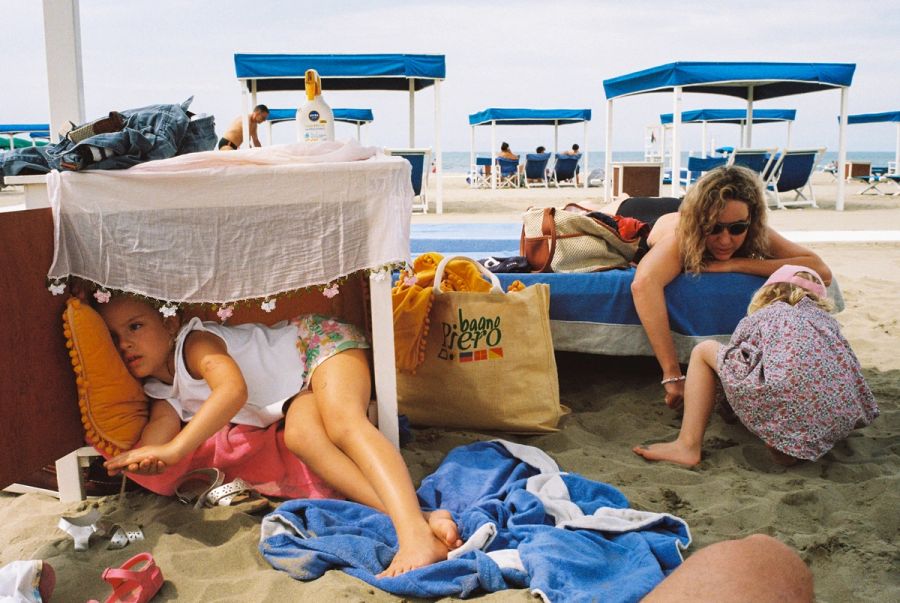 Family sheltering under a beach cabana on an Italian lido. Film photograph by Nicolò Pudel