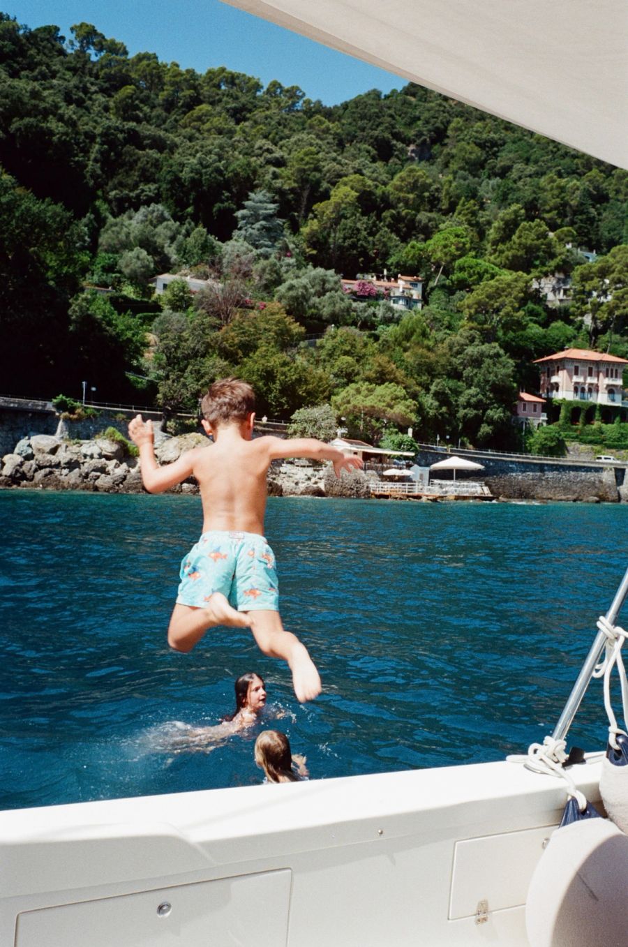 Boy in starfish swim shorts jumping from a boat into the sea, Ligurian coast, Italy. Film photograph by Nicolò Pudel