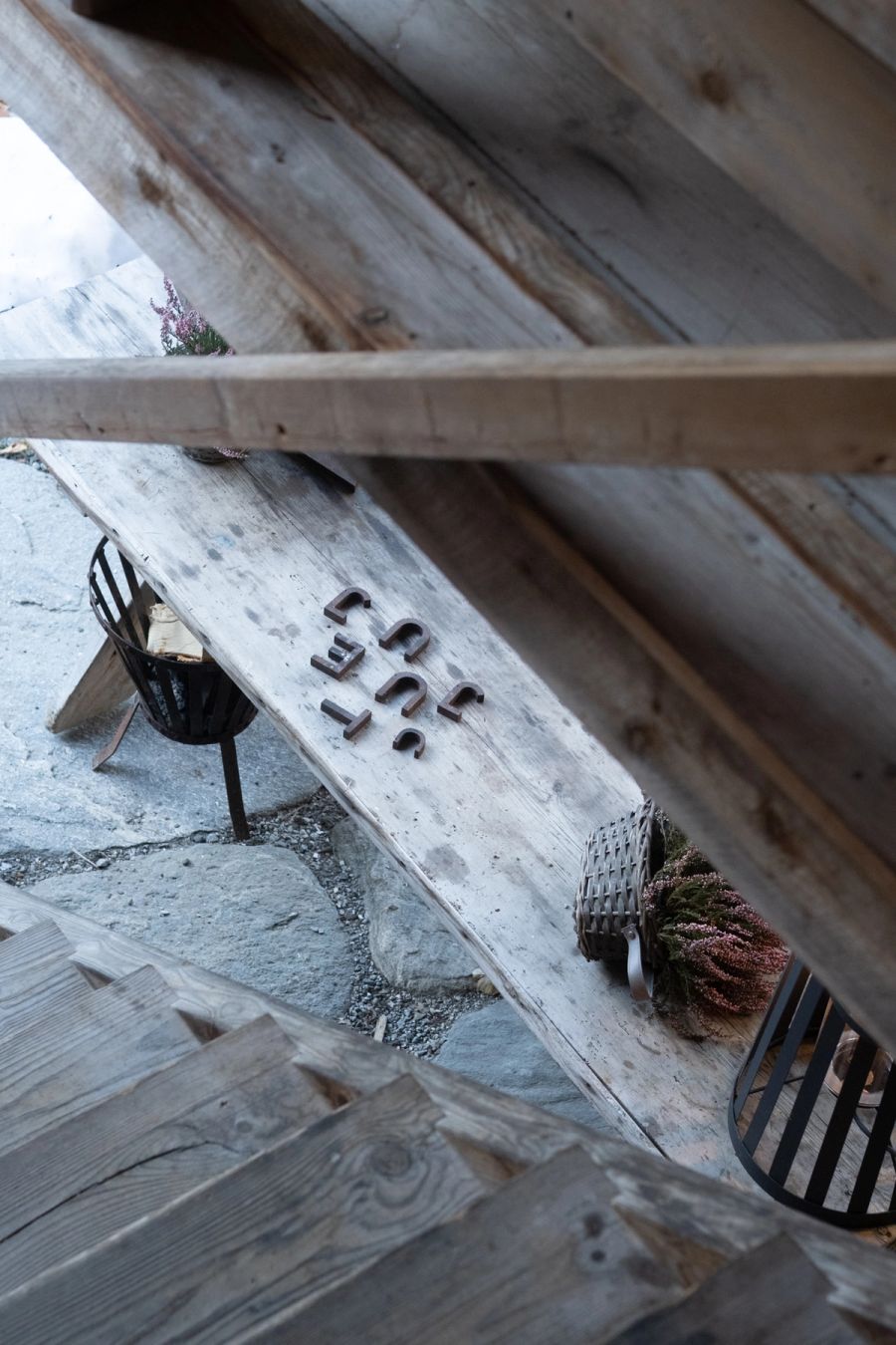 Looking down through timber rafters to a weathered bench and a fire basket, Norway. Film photograph by Nicolò Pudel