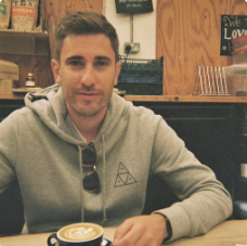 Kolekti's Associate Product Manager, Tom Carrott, sitting at a table with a coffee
