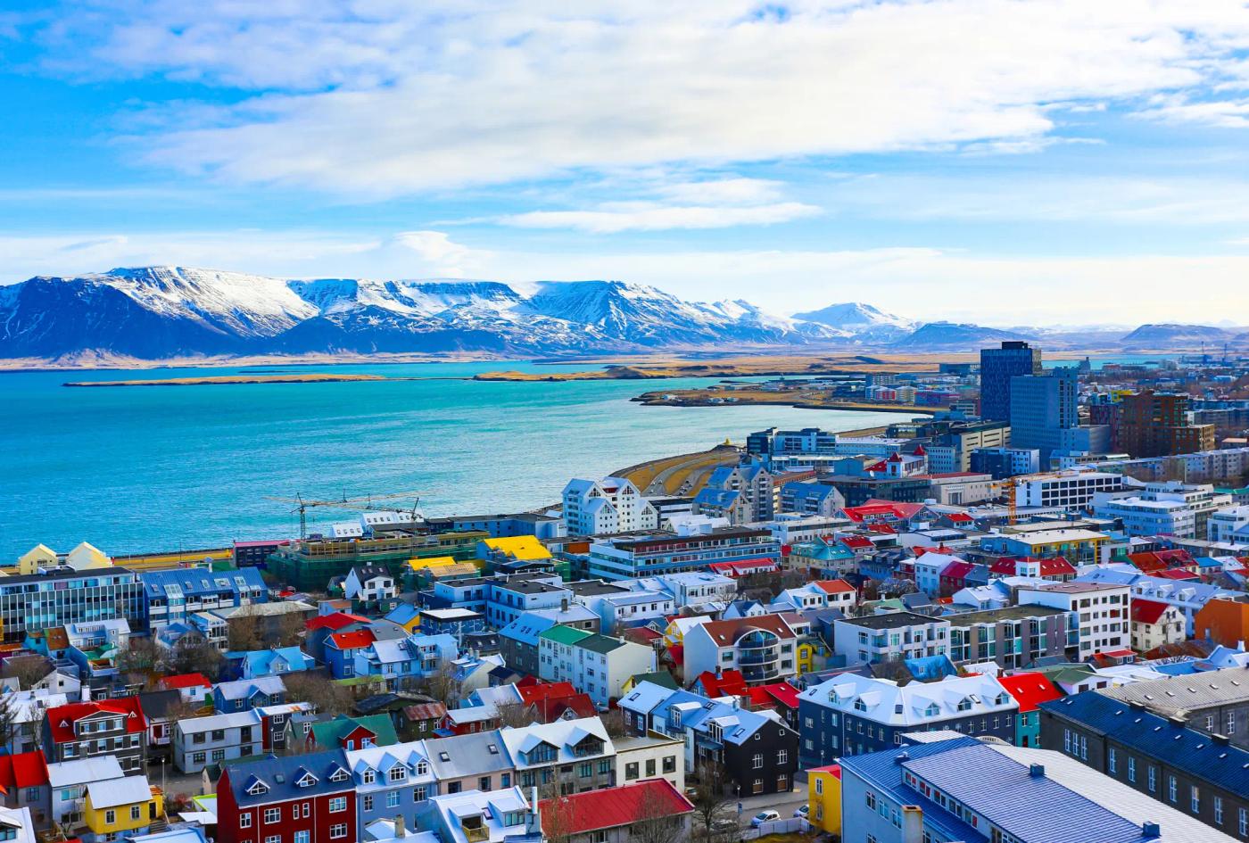 A photograph showing the city of Reykjavik beside the water with mountains in the background