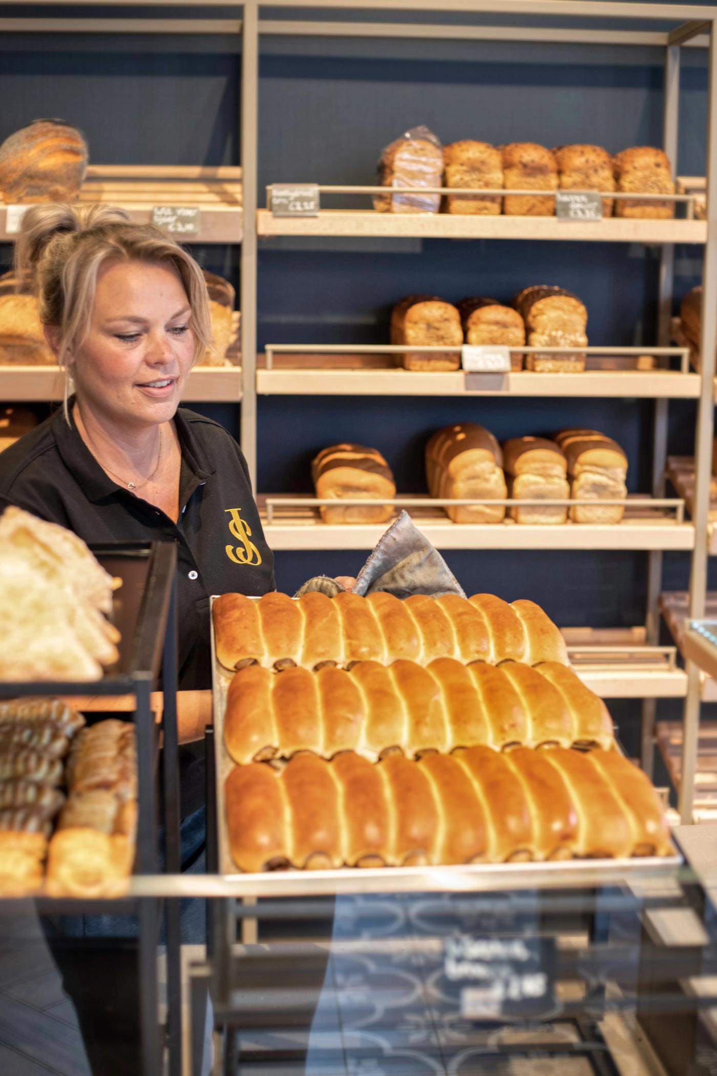 Medewerker van Warme Bakker Jac Smit met een plaat vers brood bij de broodwand.