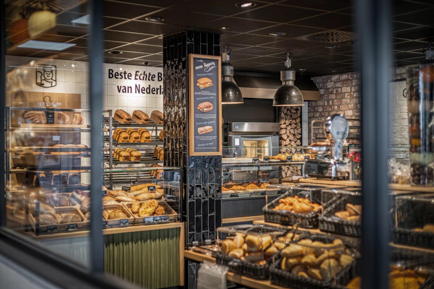 Modern winkelinterieur van Bakkerij Gommans in Horst met royale broodpresentatie, groene houten fronten, zwarte tegels en warme houtaccenten die het ambachtelijke karakter versterken.