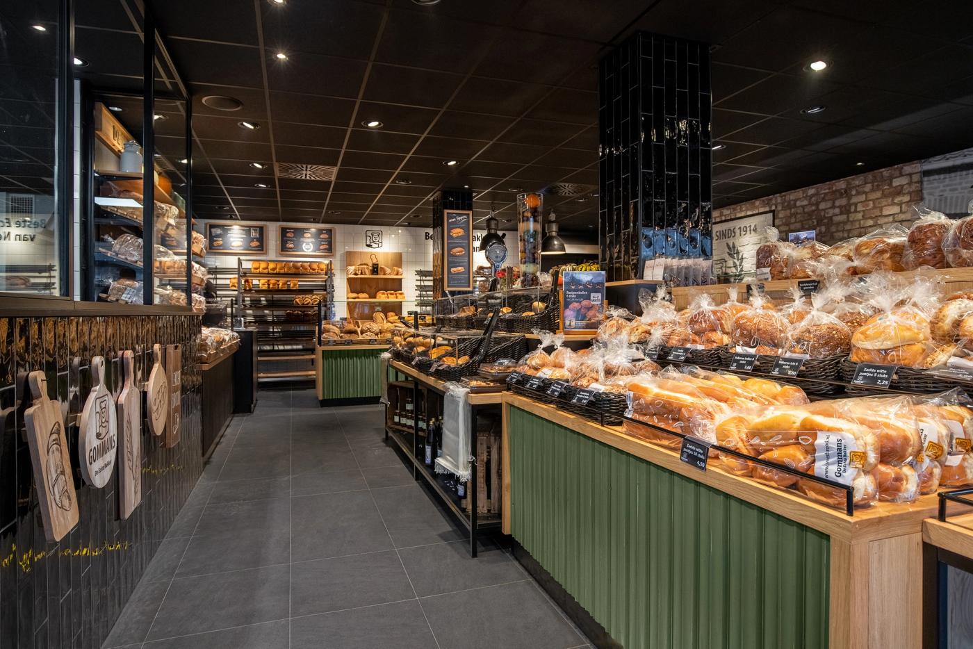 Modern winkelinterieur van Bakkerij Gommans in Horst met royale broodpresentatie, groene houten fronten, zwarte tegels en warme houtaccenten die het ambachtelijke karakter versterken.