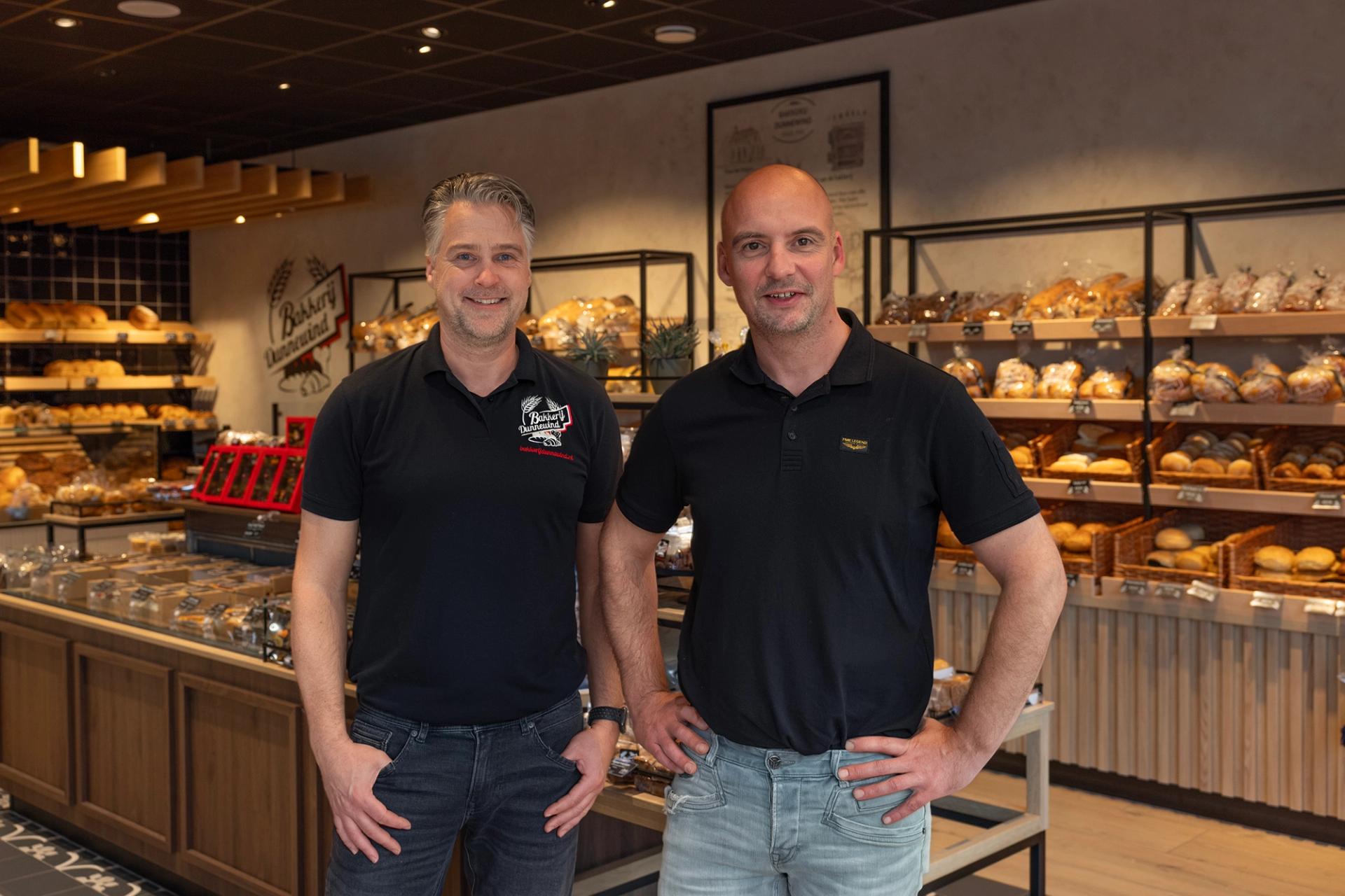 Bakkerij Dunnewind in Paterswolde-Eelde, met de ondernemers John en Alex in het vernieuwde winkelinterieur, omringd door warme houtaccenten en een uitgebreide presentatie van vers brood en banket.
