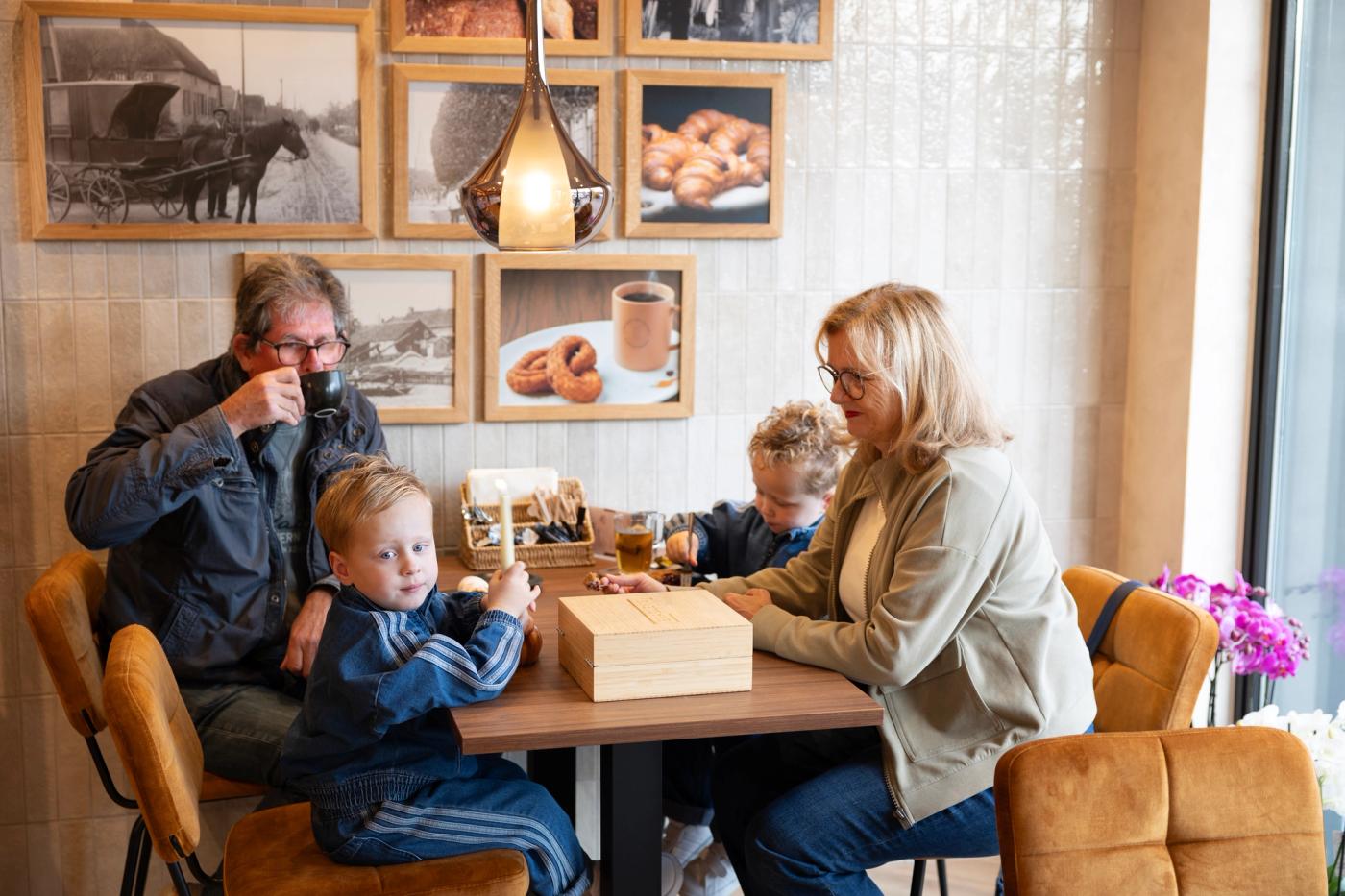 Gezellig koffiemoment met jong en oud in de sfeervolle lunchhoek van Brood- & Banketbakkerij Gerard van Keulen in Beesd, met warme zitplaatsen en historische foto’s.