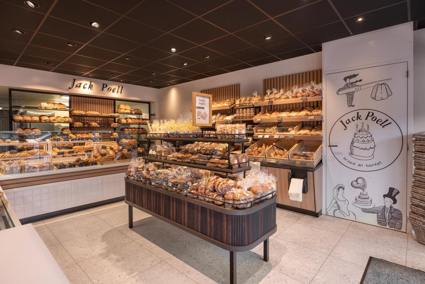 Sfeervol winkelinterieur van Bakkerij Jack Poell in Eindhoven, met ambachtelijke broodpresentaties, centraal productmeubel, warme houtaccenten en speelse bakkerijillustraties in het maatwerk interieur van Infrashop.