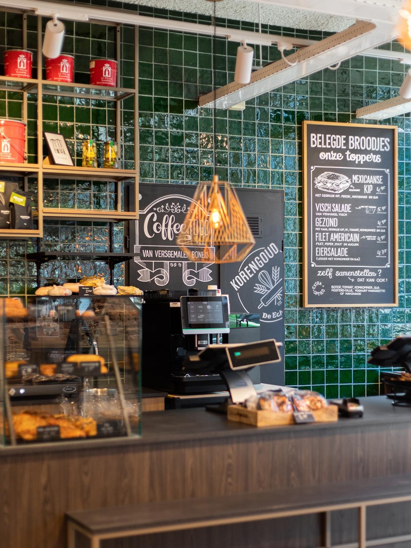 Koffiehoek met krijtborden en groene tegels bij Korengoud De Echte Bakker.
