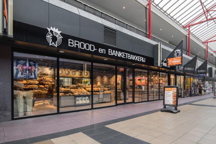 “Entree en winkelpui van Brood- en Banketbakkerij Prins in Flevoland, met een moderne zwarte gevel en zicht op de sfeervolle bakkerij en uitgebreide broodpresentatie.”