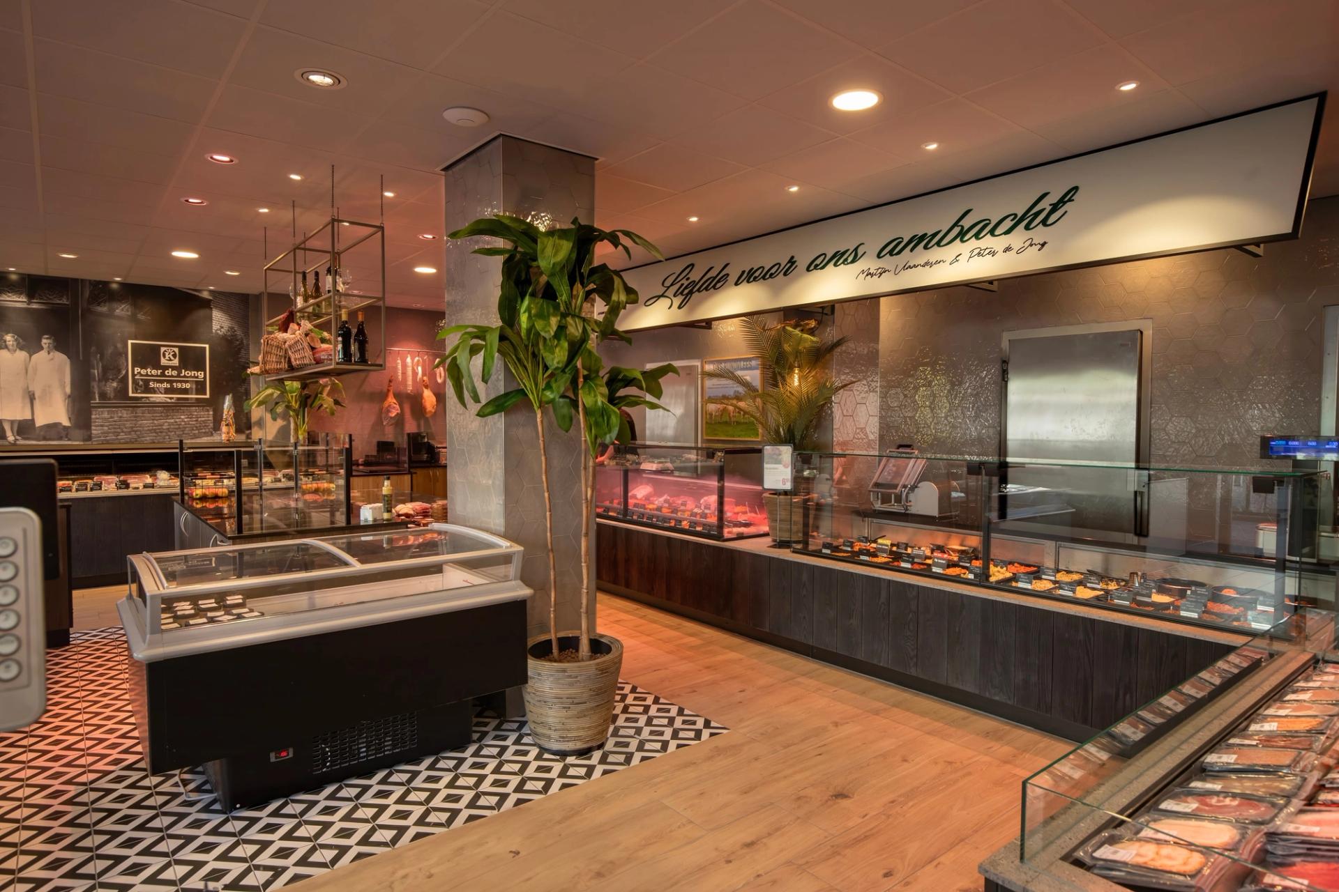 Winkelinterieur van Keurslagerij Peter de Jong in Huizen, met vleestoonbanken, een vrieskist en een palm op een zwart-wit tegelvloer.
