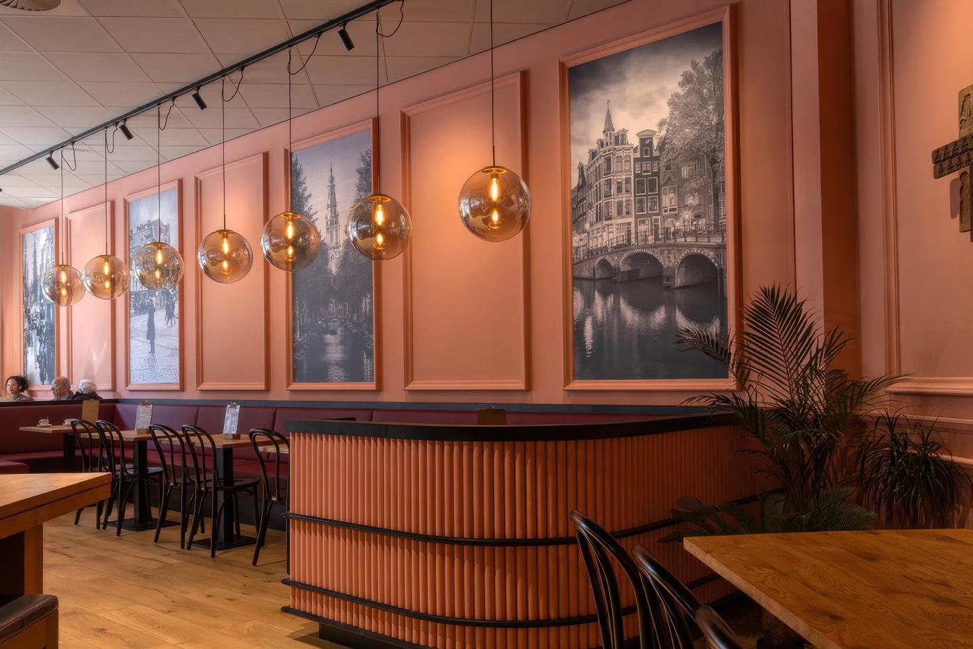 “Historische zwart-witfoto’s van Amsterdam als sfeervolle wanddecoratie in de lunchroom van Patisserie Kwekkeboom, gecombineerd met warme roze tinten, houten tafels en klassieke hanglampen.”