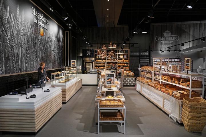 Interieur van Echte Bakker Hagedoren in Beek, Limburg, met moderne brood- en gebakspresentaties, warme houtaccenten, industriële verlichting en een grote wandvisual die het ambachtelijke karakter van de bakkerij benadrukt.