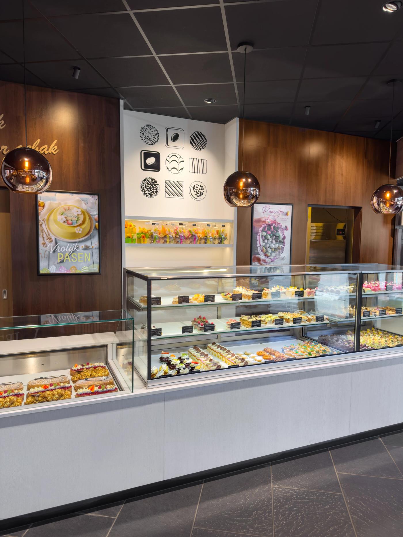 Luxe gebakpresentatie bij Bakkerij Olsthoorn in Naarden, met gekoelde vitrines vol kleurrijke patisserie, taarten en gebak in een modern winkelinterieur met warme houtaccenten.