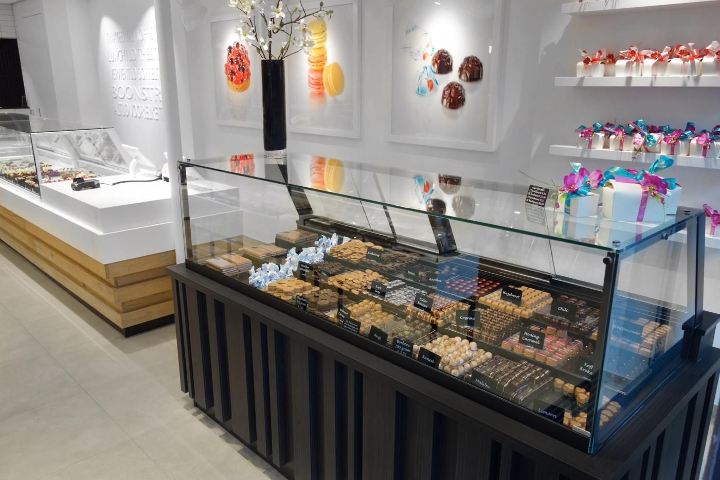 Gebaksvitrine met bonbons en een wand met chocoladecadeaus bij Banketbakkerij Boonstra.