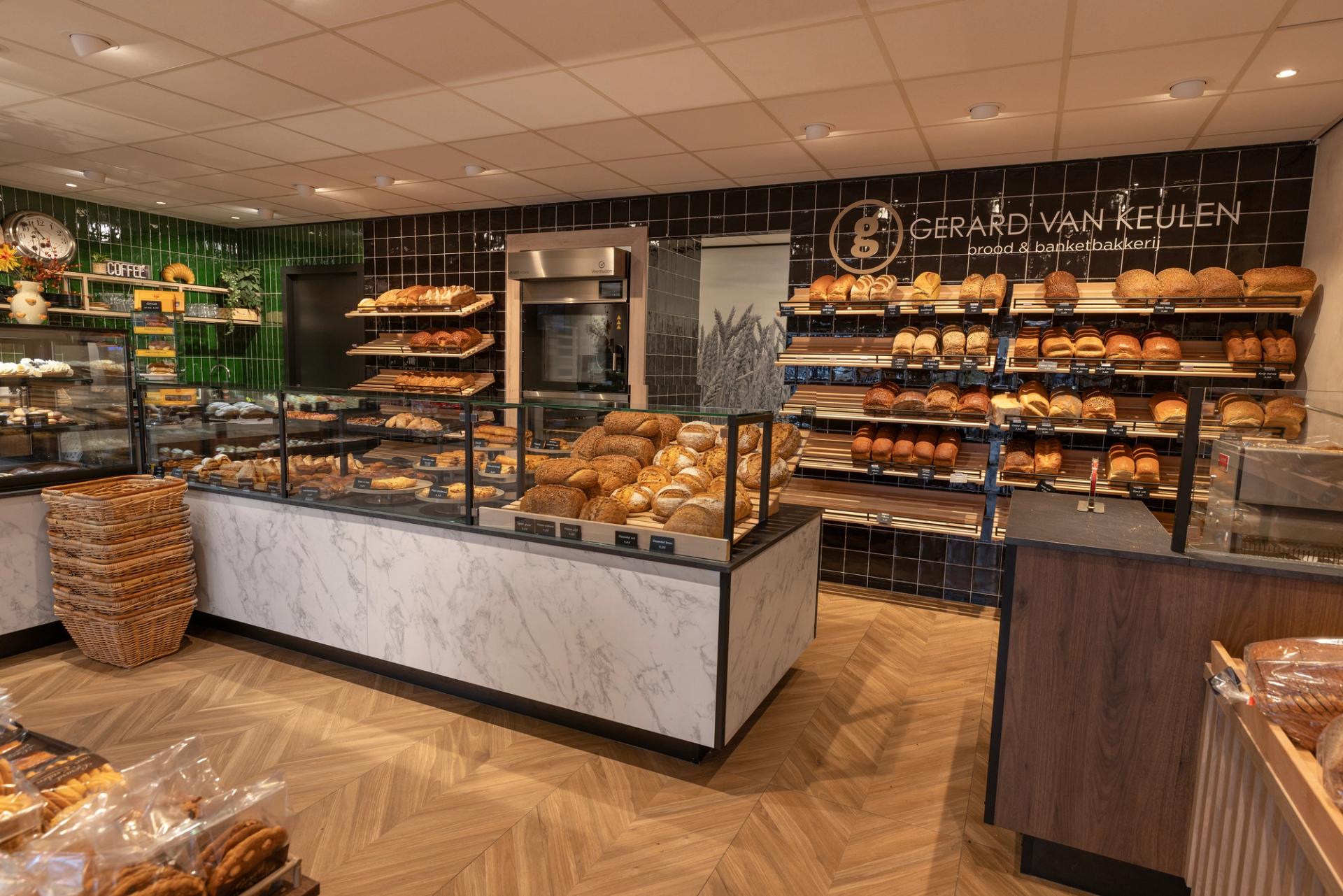 Modern winkelinterieur gemaakt door Infrashop van Brood- & Banketbakkerij Gerard van Keulen in Beesd, met luxe brood- en gebakspresentaties, warme houtaccenten, marmerlook toonbanken en groene en zwarte wandtegels.