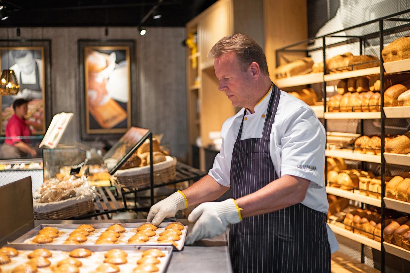 Bakker legt vers gebak op een bakplaat bij de broodwand van Bakker Hulleman.