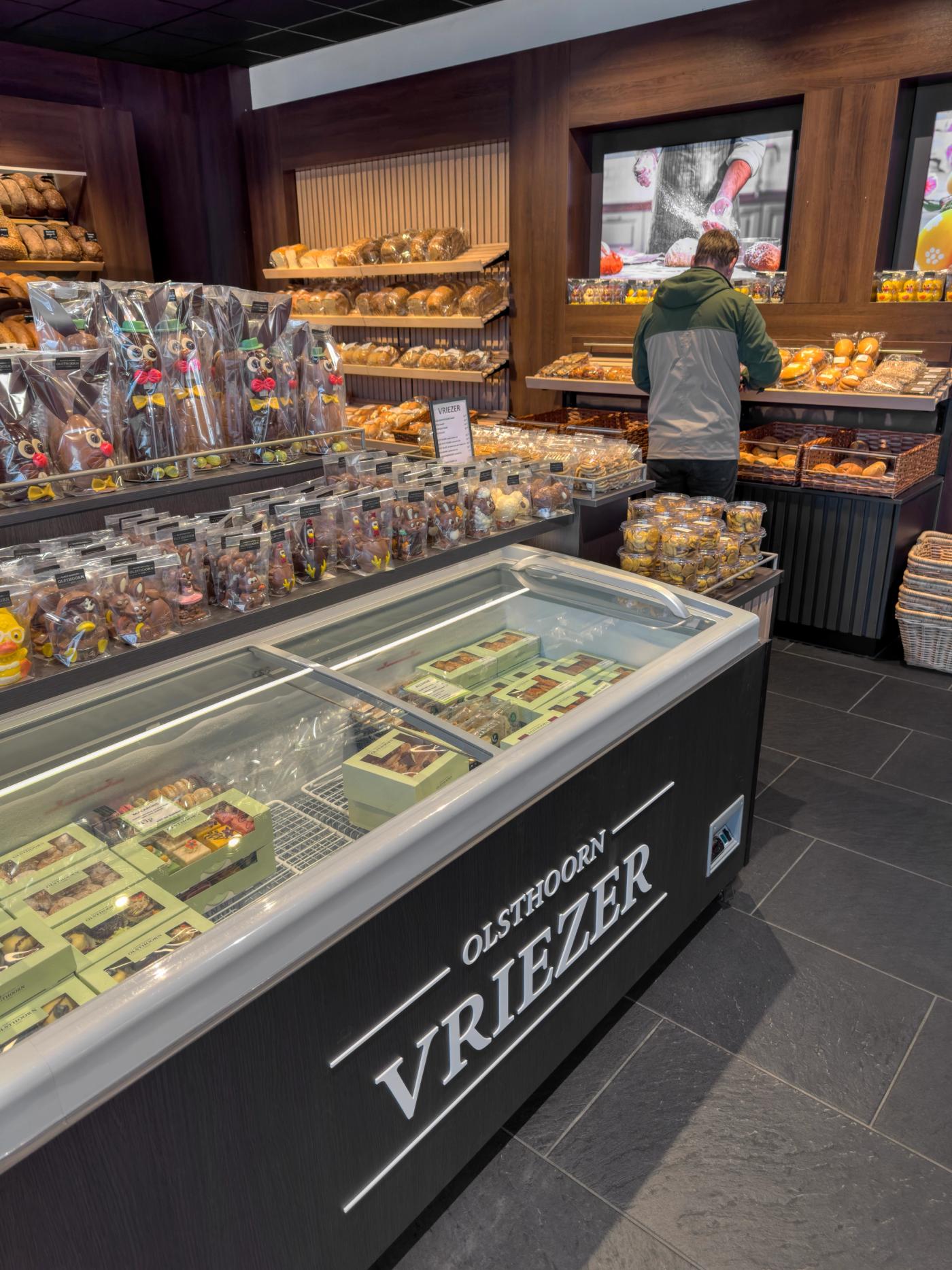 Winkelinterieur van Bakkerij Olsthoorn in Naarden, met geïntegreerde vriezer voor luxe chocoladeproducten, opvallende chocoladepresentatie en ambachtelijke broodafdeling met warme houtaccenten.