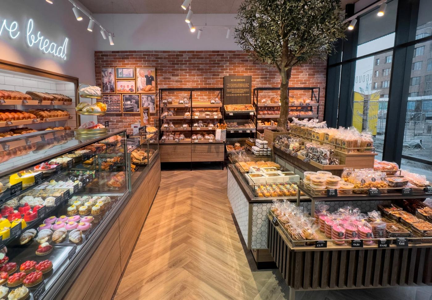 Overzicht van de winkel van Korengoud in Rosmalen, met gebaksvitrines, broodtafels en een bakstenen wand.