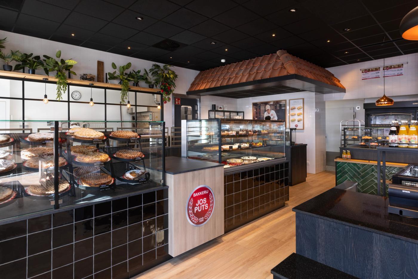 Sfeervol winkelinterieur van Bakkerij Jos Puts in Echt, met royale vlaaien- en gebakspresentatie, zwarte tegels, warme houtaccenten en maatwerk interieur van Infrashop.