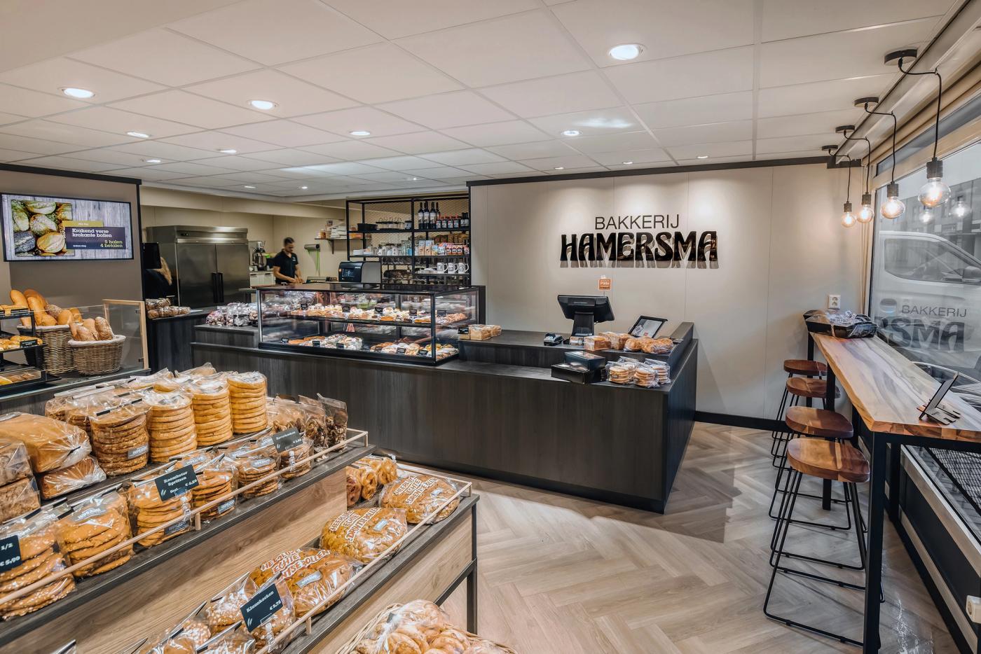Modern winkelinterieur van Bakkerij Hamersma in Grootegast, met ruime brood- en banketpresentaties, donkere toonbanken, warme houtaccenten en een gezellige koffiebar langs de winkelpui.