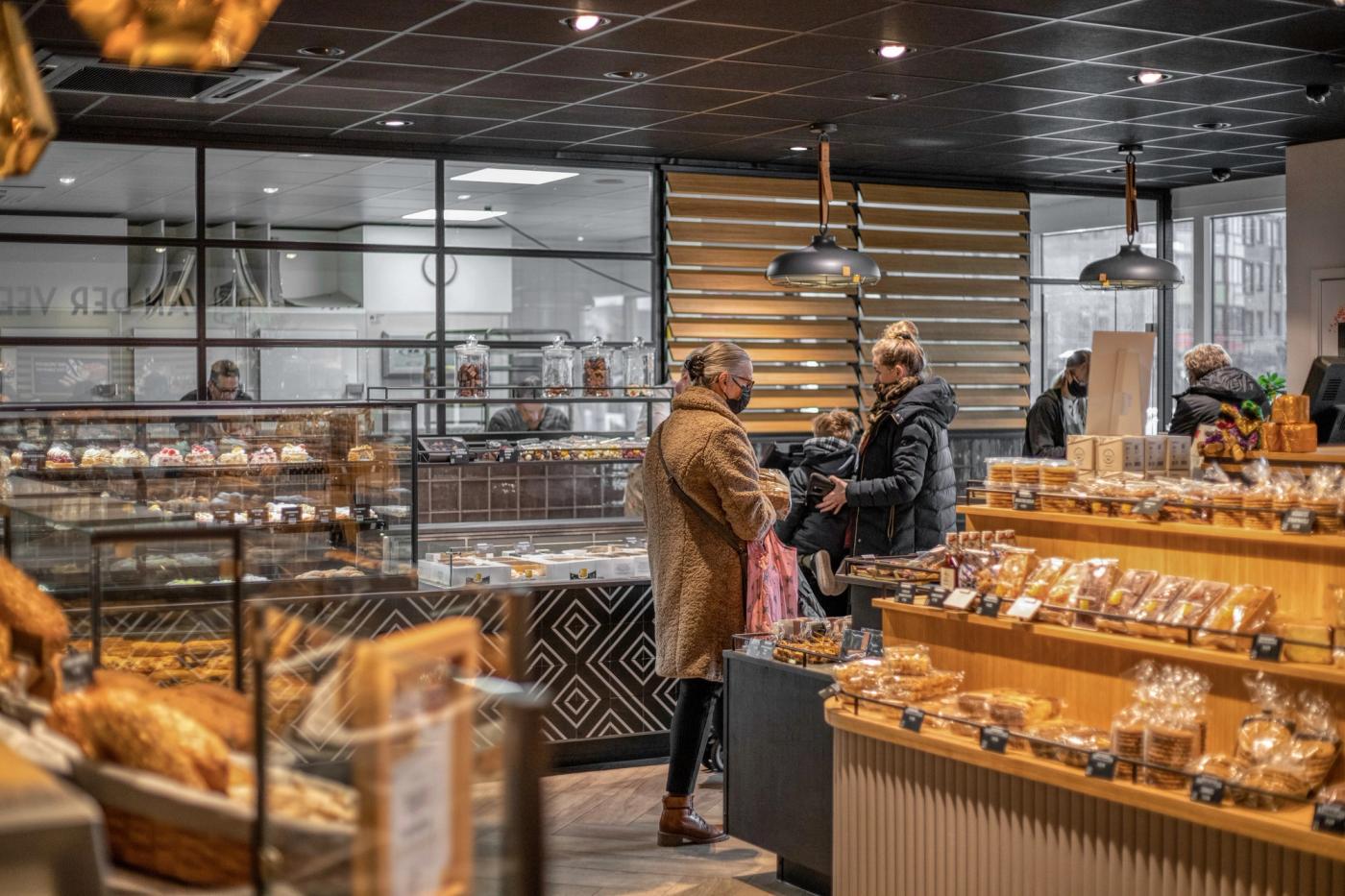 Klanten bij de toonbank van Bakker Van der Veer, met zicht op de bakkerij achter glas.