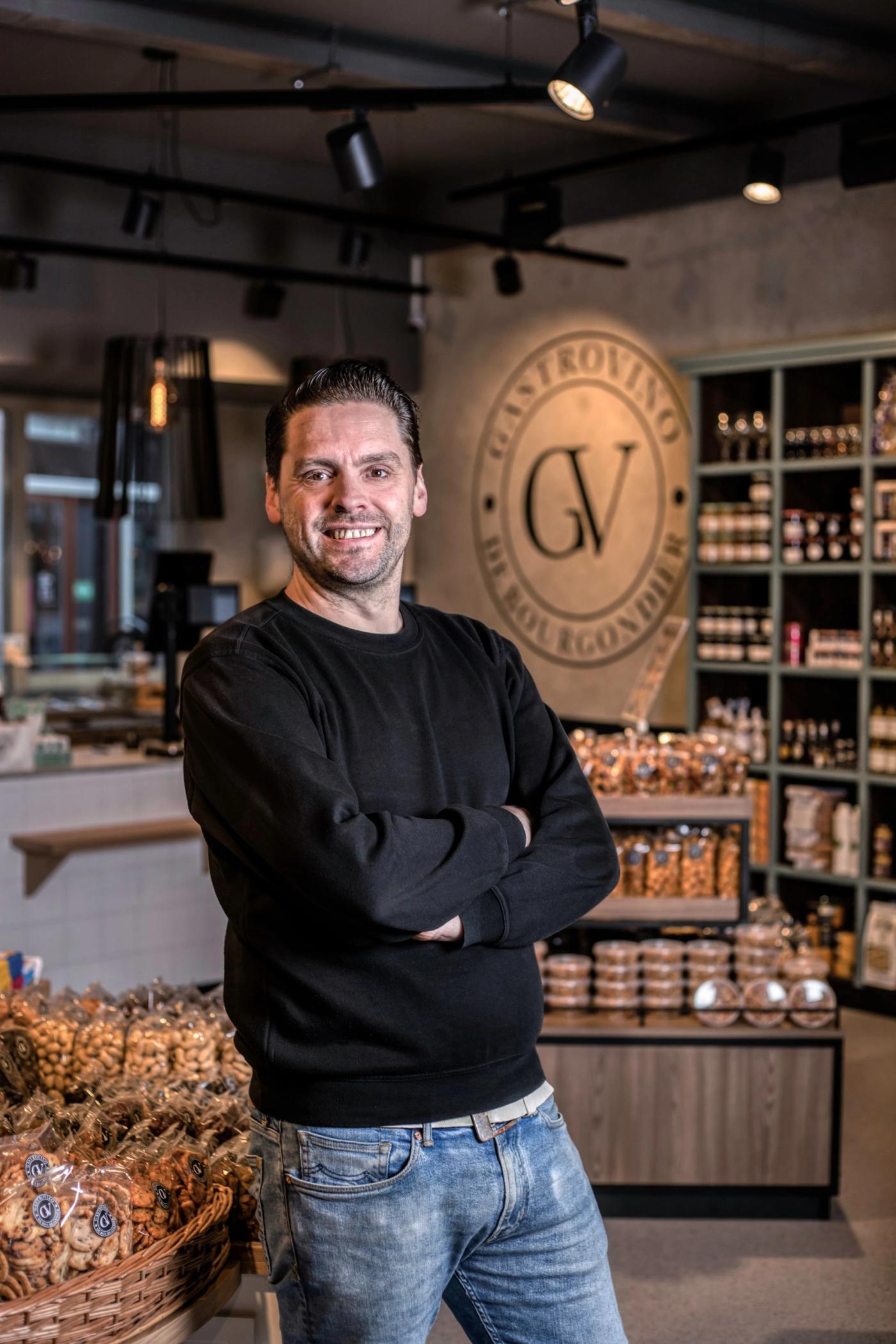 Medewerker in de winkel van Gastrovino De Bourgondiër in Ermelo, met het GV-logo op de wand.