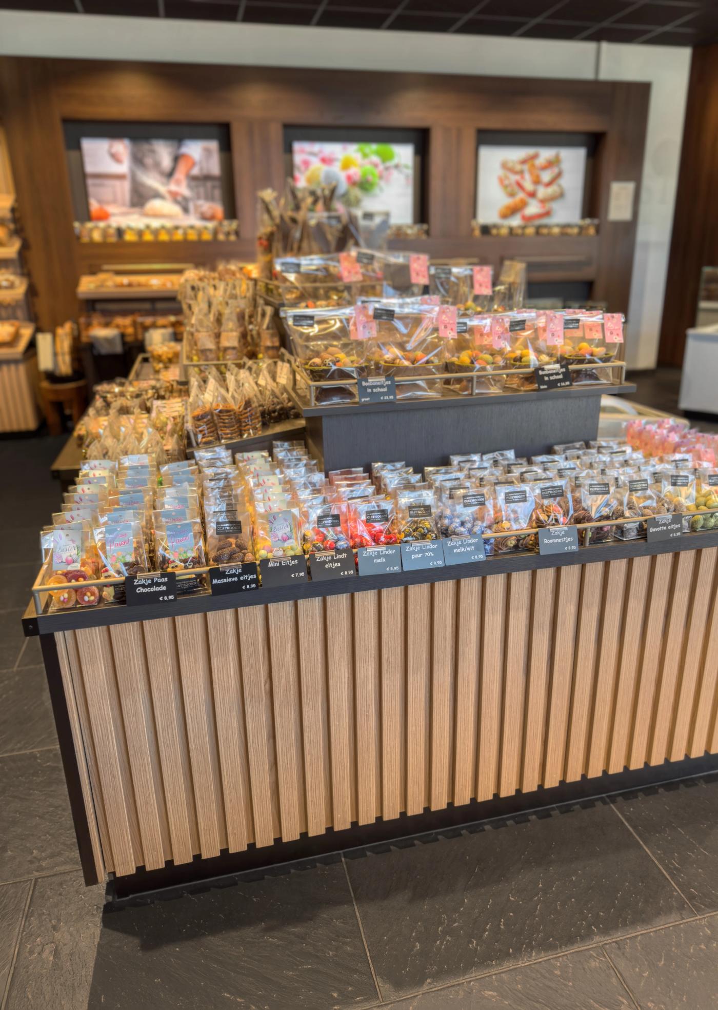 Sfeervolle chocolade- en zoetwarenpresentatie bij Bakkerij Olsthoorn in Naarden, met luxe verpakte bonbons en lekkernijen op een stijlvol houten presentatie-eiland.