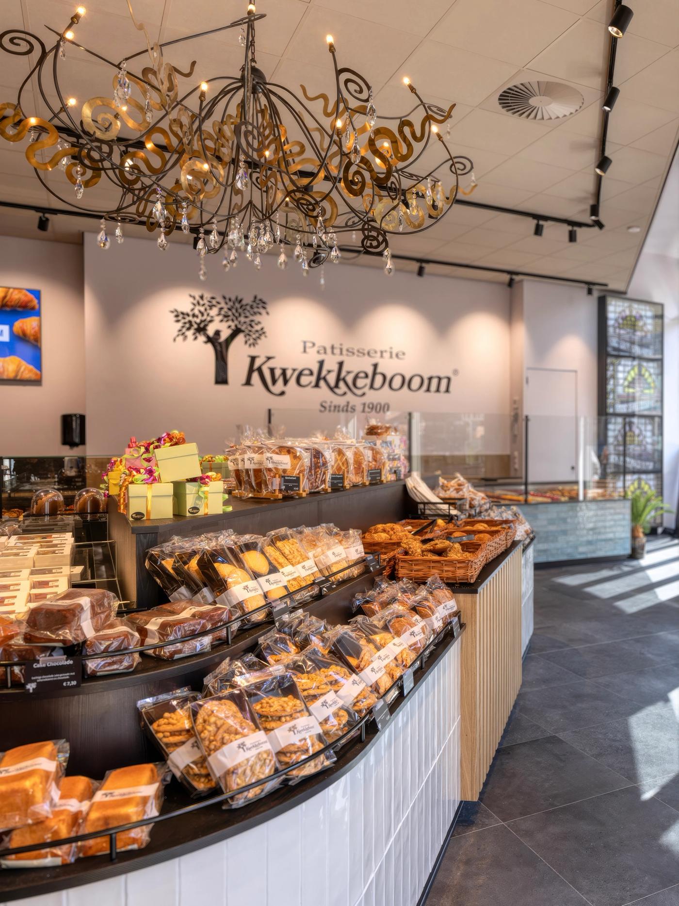 “Interieur van Patisserie Kwekkeboom in Amsterdam met ronde productpresentatie vol ambachtelijke koek en banket, sfeervolle kroonluchter en warme winkelinrichting, ontworpen en gebouwd door Infrashop.”