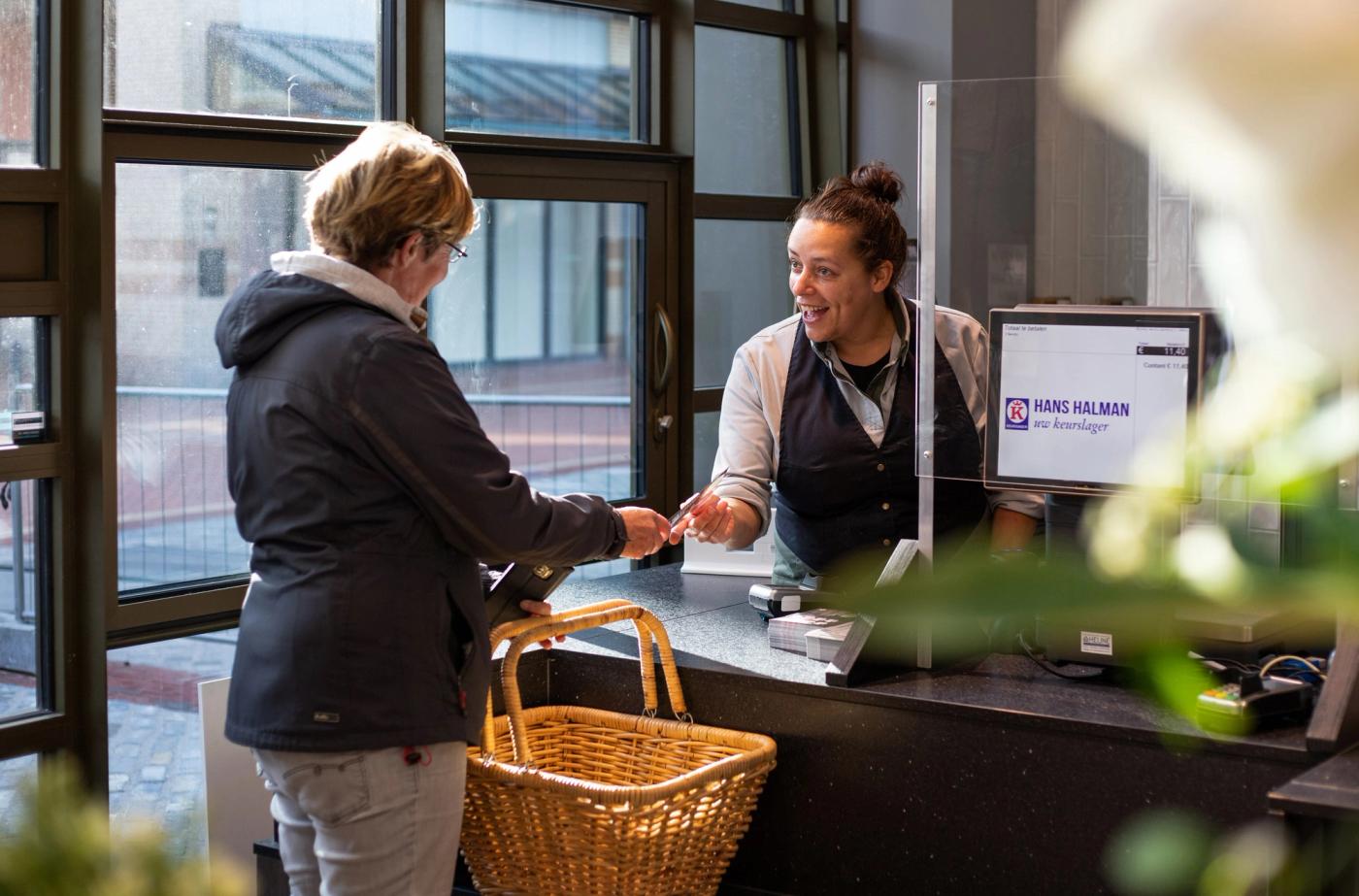 Medewerker helpt een klant met een boodschappenmand aan de kassa bij Keurslagerij Hans Halman.
