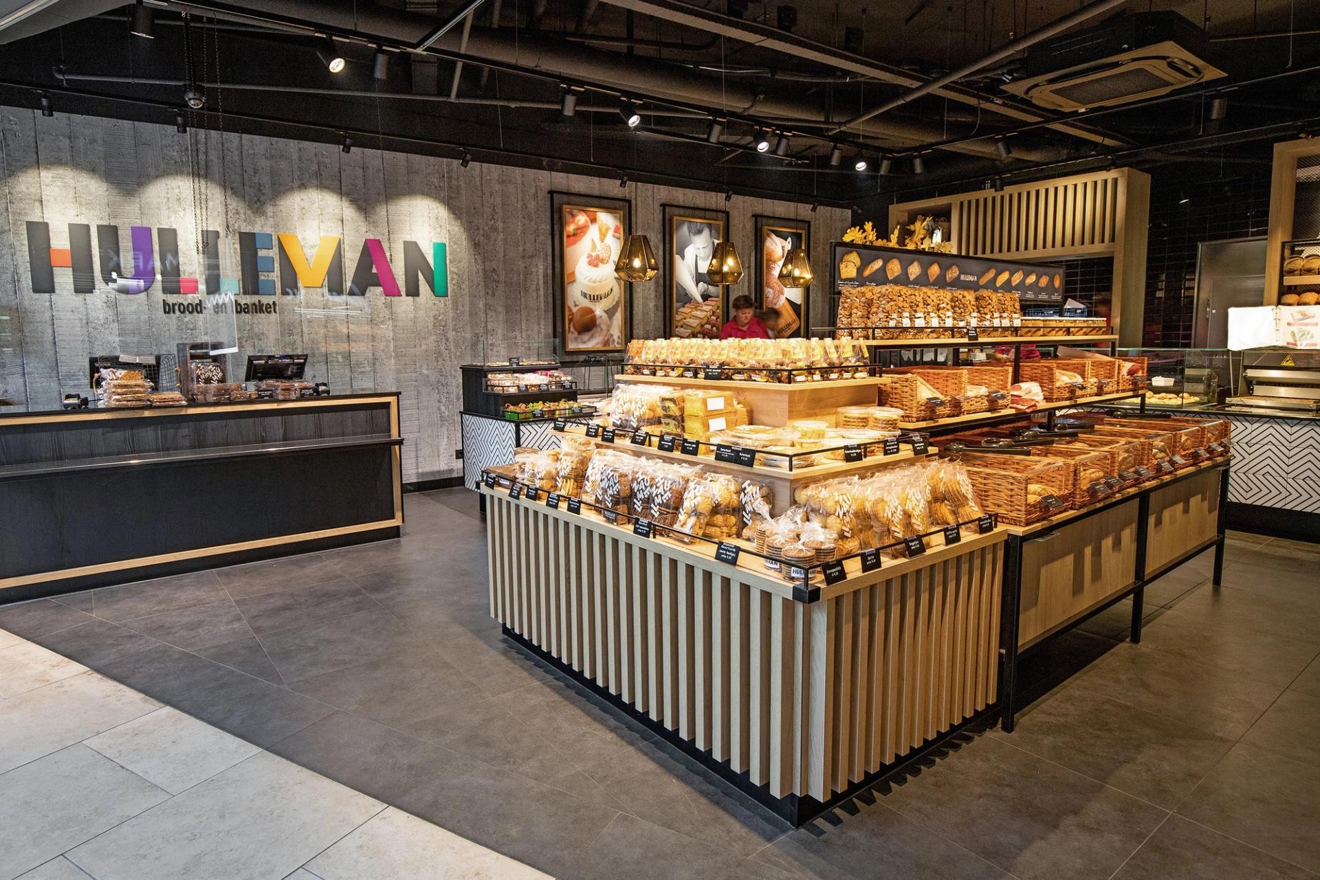Winkelinterieur van Bakker Hulleman in Amstelveen, met een middenmeubel vol brood en de kleurrijke Hulleman-letters op de wand.