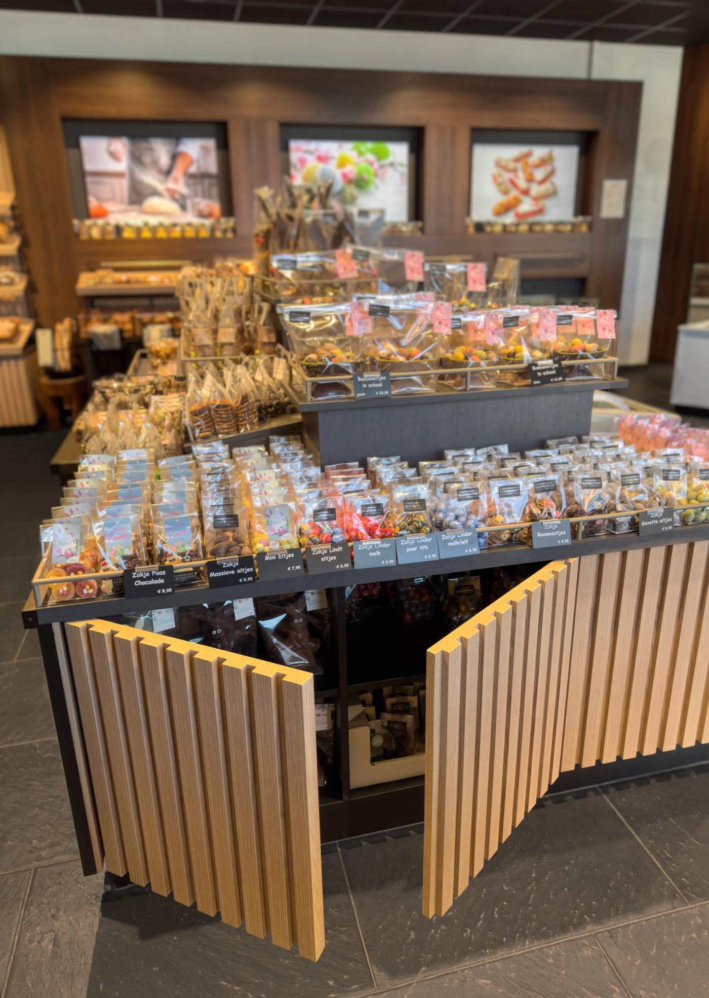 Sfeervolle chocolade- en zoetwarenpresentatie bij Bakkerij Olsthoorn in Naarden, met luxe verpakte bonbons en lekkernijen op een stijlvol houten presentatie-eiland.