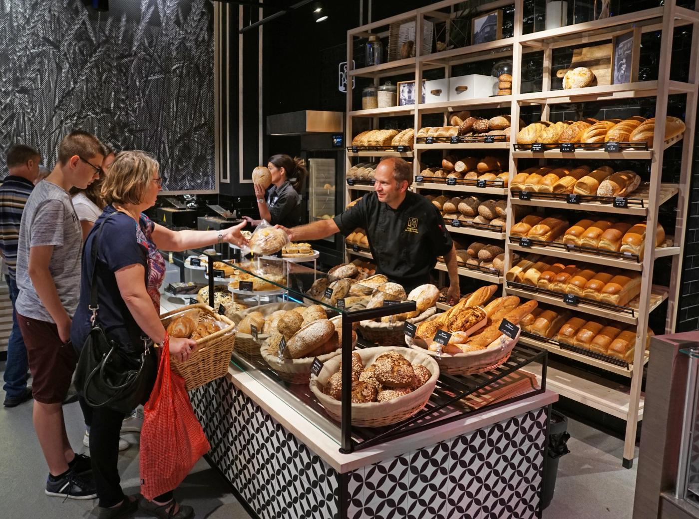 Peter Hagedoren helpt persoonlijk een klant bij de broodpresentatie van Echte Bakker Hagedoren in Beek, omringd door een ruime keuze aan versgebakken ambachtelijke broden.