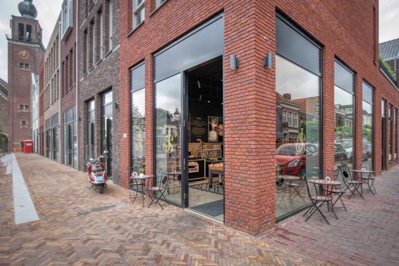 Gevel van Warme Bakker Jac Smit op een hoek in Zevenbergen, met terras en grote ramen.