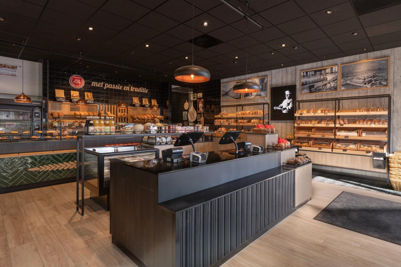 Compleet winkelinterieur van Bakkerij Jos Puts in Echt, met ambachtelijke broodpresentatie, vitrines, warme houtaccenten, groene tegels en industriële details.