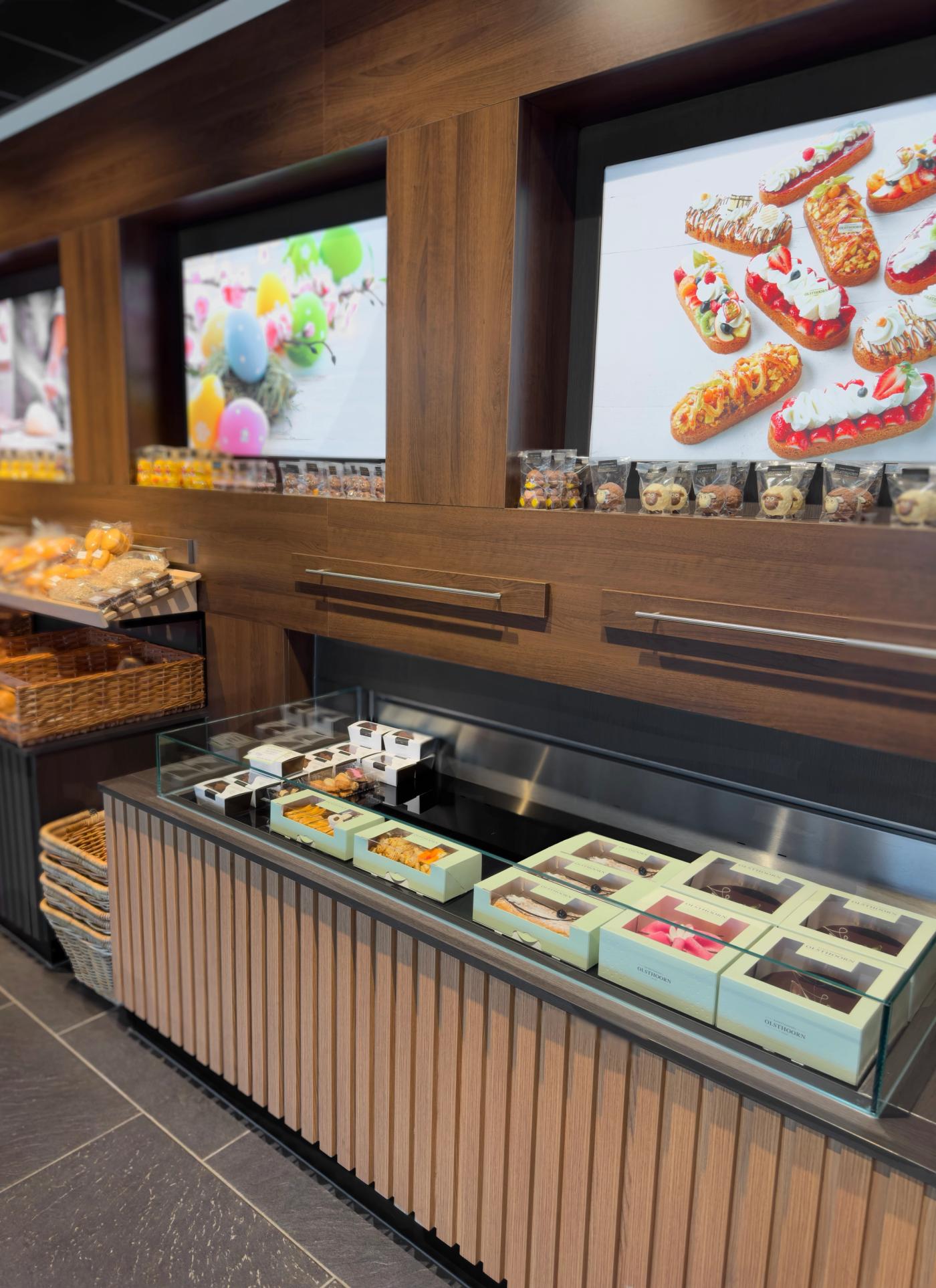 Stijlvolle productpresentatie bij Bakkerij Olsthoorn in Naarden, met luxe verpakte chocolade en gebak, warme houtaccenten en verlichte sfeerbeelden in het winkelinterieur.