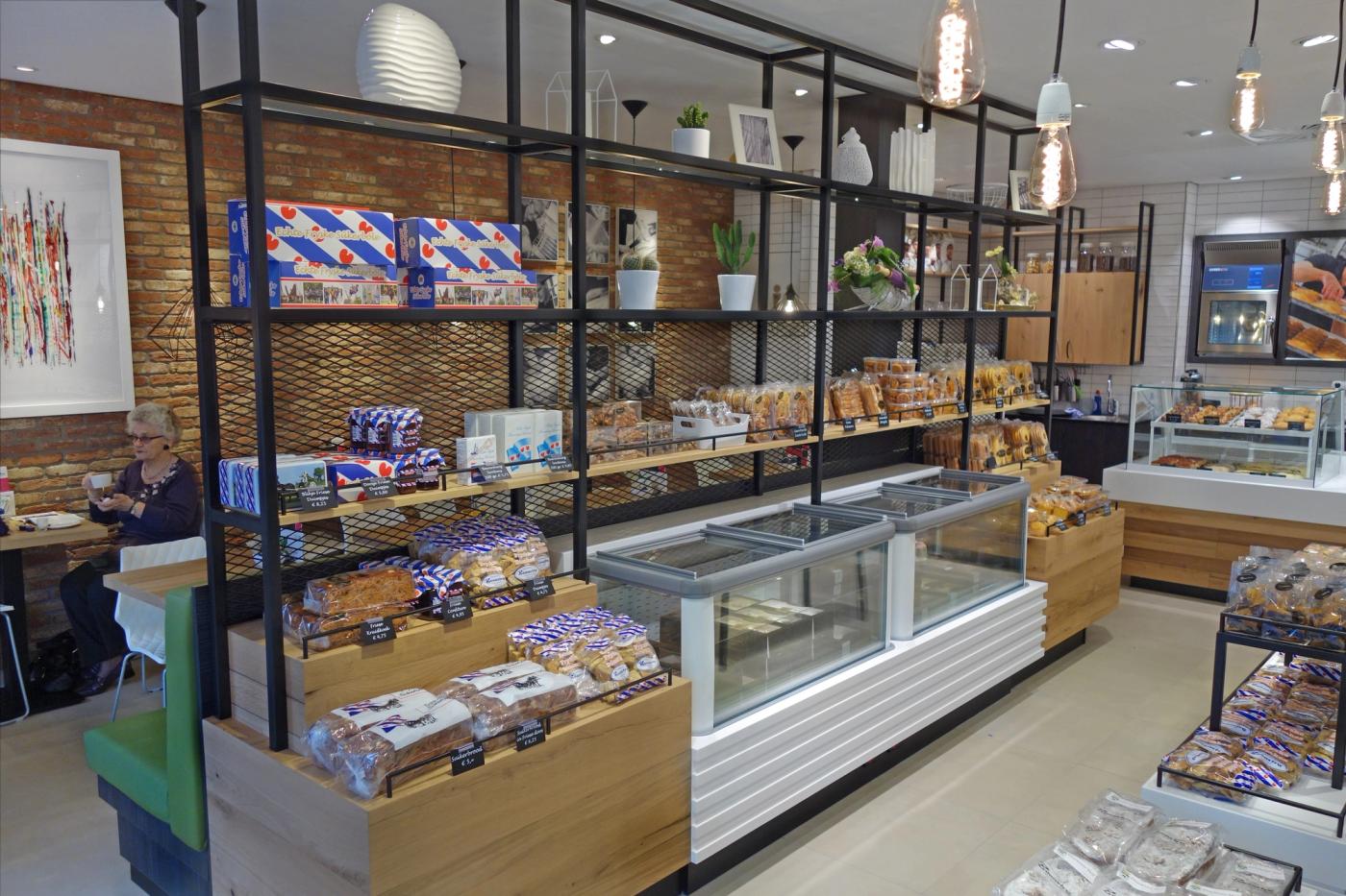 Wandschappen met koek en banket bij Banketbakkerij Boonstra, met zitplekken op de achtergrond.