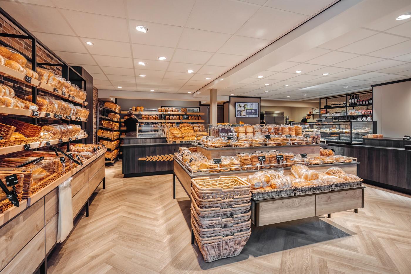 Uitgebreide broodpresentatie bij Bakkerij Hamersma in Grootegast, met ambachtelijke broden, warme houtaccenten, bakstenen wanden en maatwerk winkelmeubilair ontworpen door Infrashop.