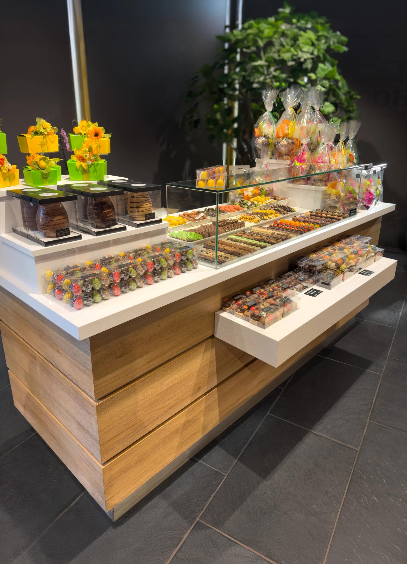 Luxe chocoladepresentatie bij Bakkerij Olsthoorn in Naarden, met kleurrijke bonbons, paaseieren en chocoladecadeaus stijlvol gepresenteerd op een modern houten presentatie-meubel.