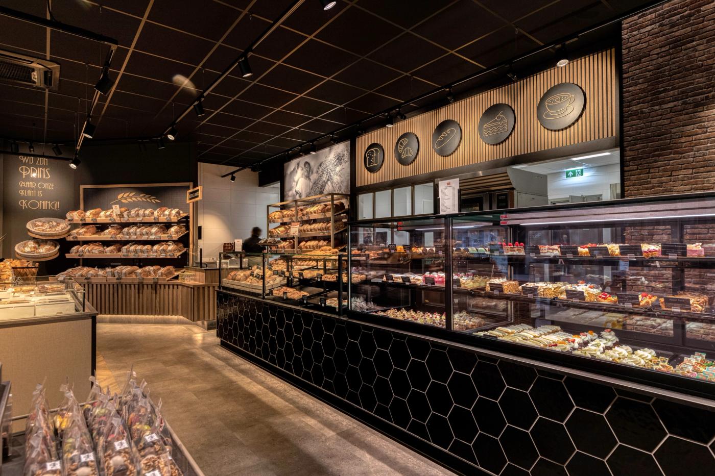 “Modern winkelinterieur van Brood- en Banketbakkerij Prins in Flevoland met ambachtelijke broodpresentatie, zwarte tegels, warme houtaccenten en sfeervolle verlichting.”