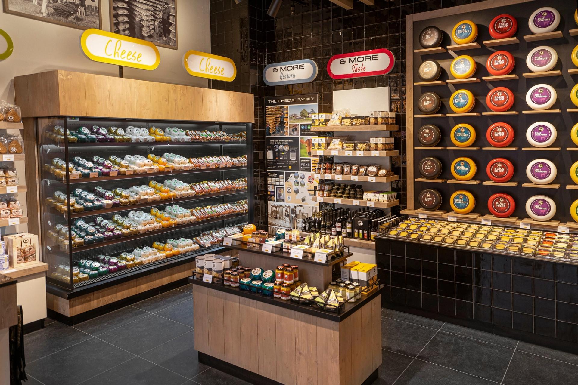 Winkelinterieur van Cheese & More in de Mall of the Netherlands in Leidschendam, met een wand vol kleurrijke kazen, verlichte vitrines en houten presentatiemeubels.