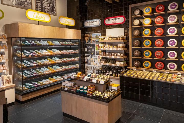 Winkelinterieur van Cheese & More in de Mall of the Netherlands in Leidschendam, met een wand vol kleurrijke kazen, verlichte vitrines en houten presentatiemeubels.