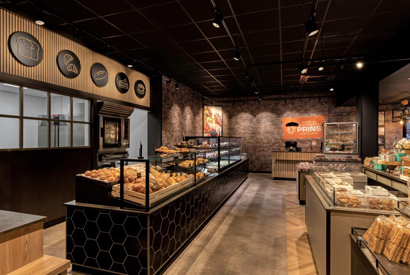 “Modern winkelinterieur van Brood- en Banketbakkerij Prins in Flevoland met ambachtelijke broodpresentatie, zwarte tegels, warme houtaccenten en sfeervolle verlichting.”