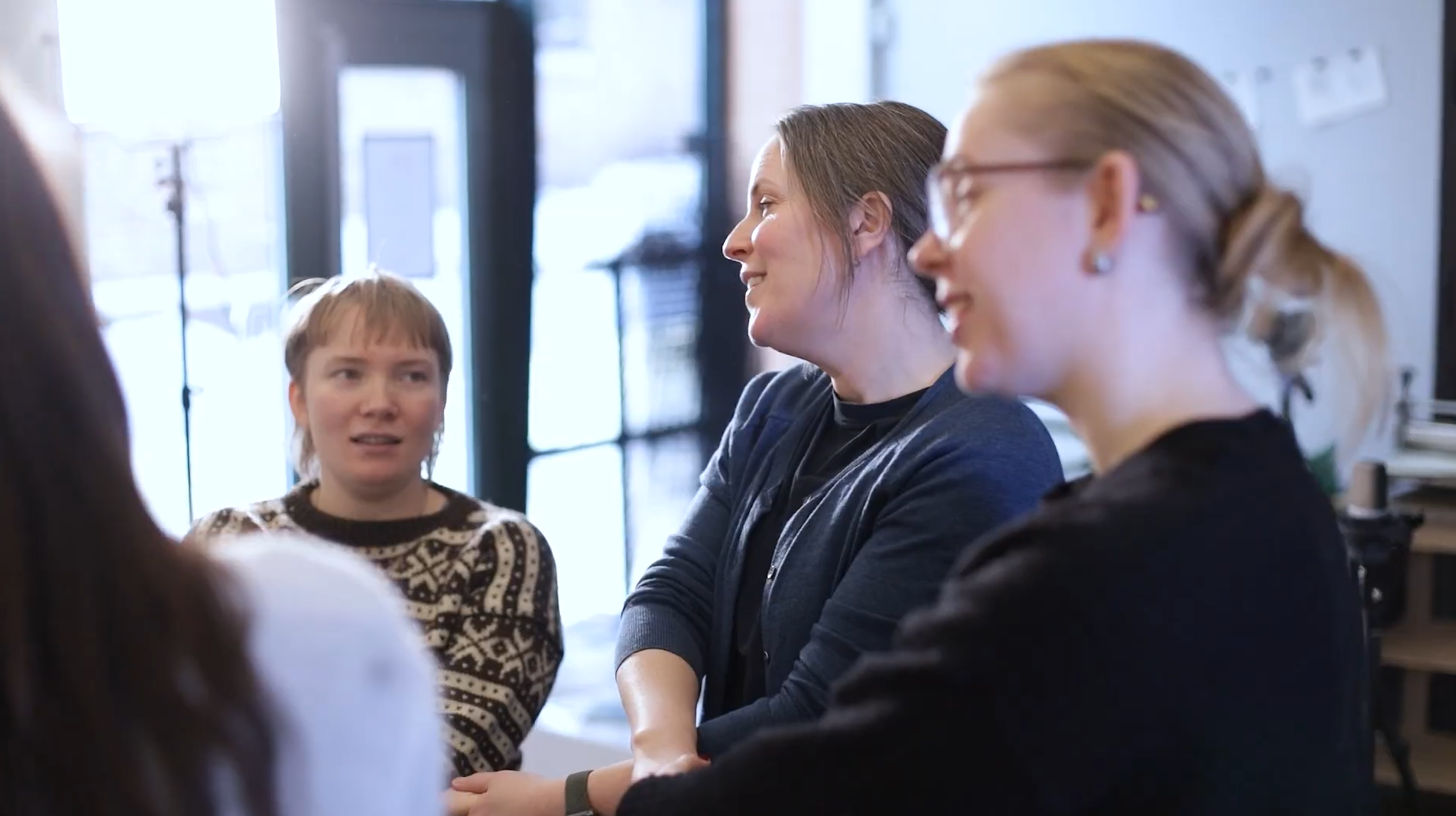 Utsnitt av personer som står i ring og holder hender i kryss.