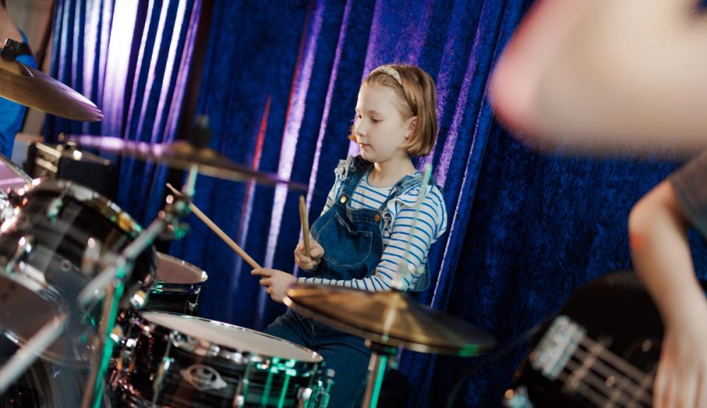 En jente spiller på trommesett på et musikkrom