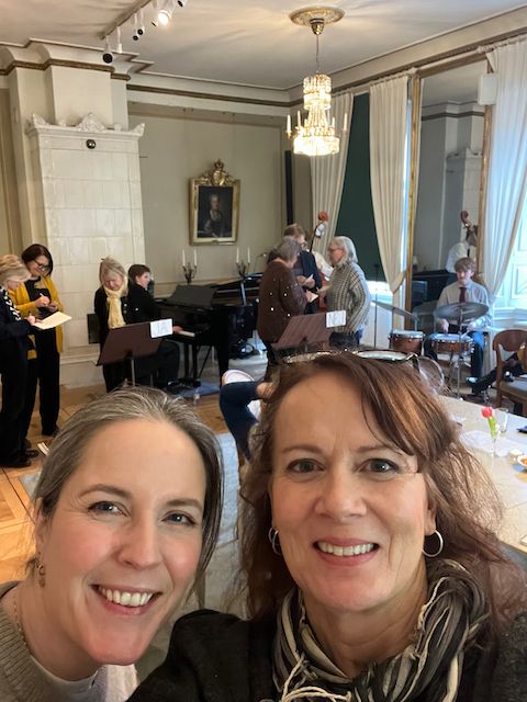 Silje og Ulrika tar en selfie med møterommet og nettverksmedlemmer i bakgrunnen